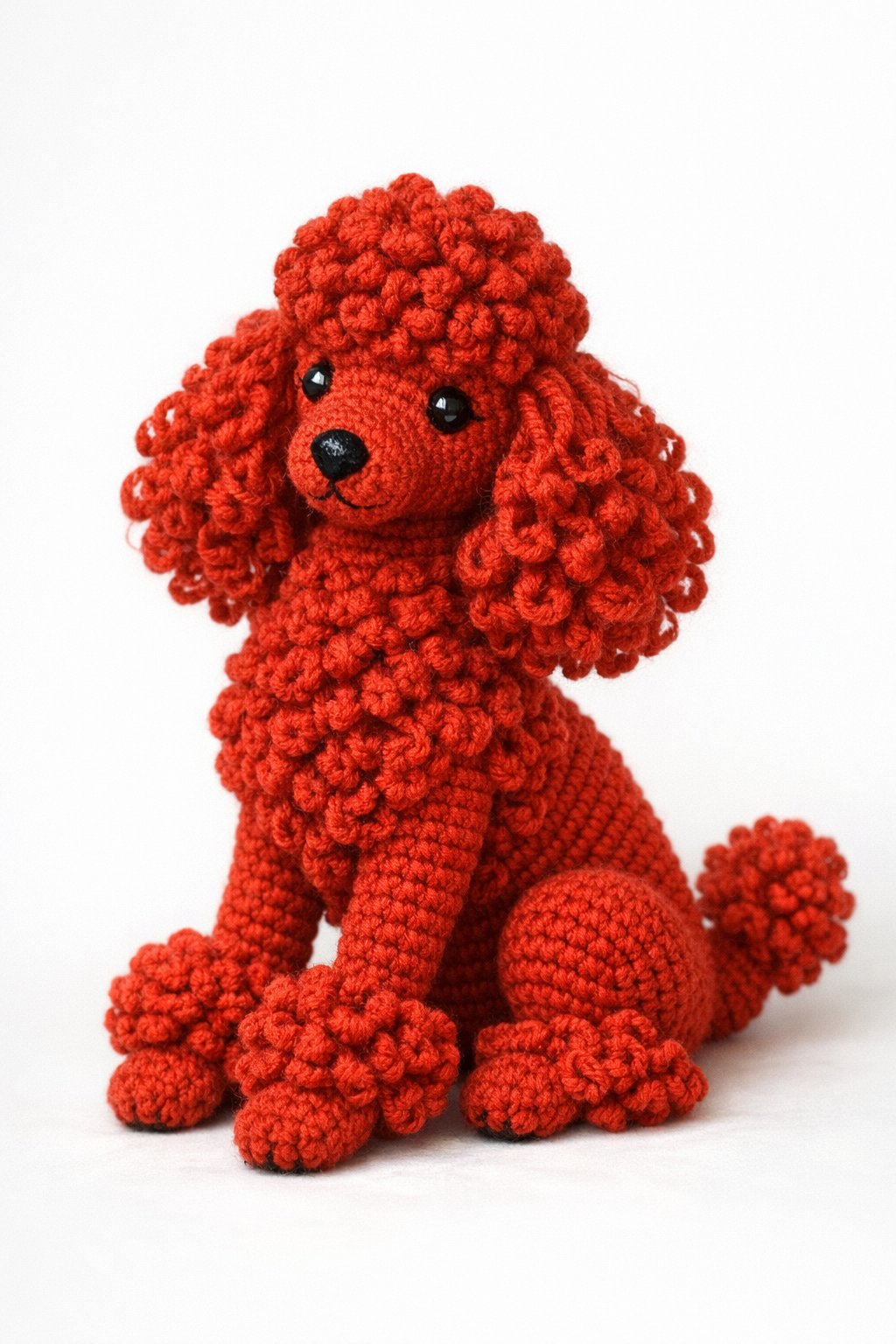 A realistic red crocheted poodle dog with curly fur sitting on a plain background.